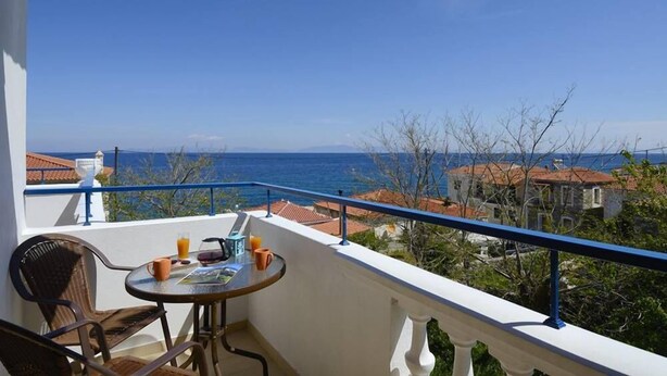A balcony with a table and chairs, overlooking a coastal view with buildings and the sea. - Zafiria Apartments (Samos)