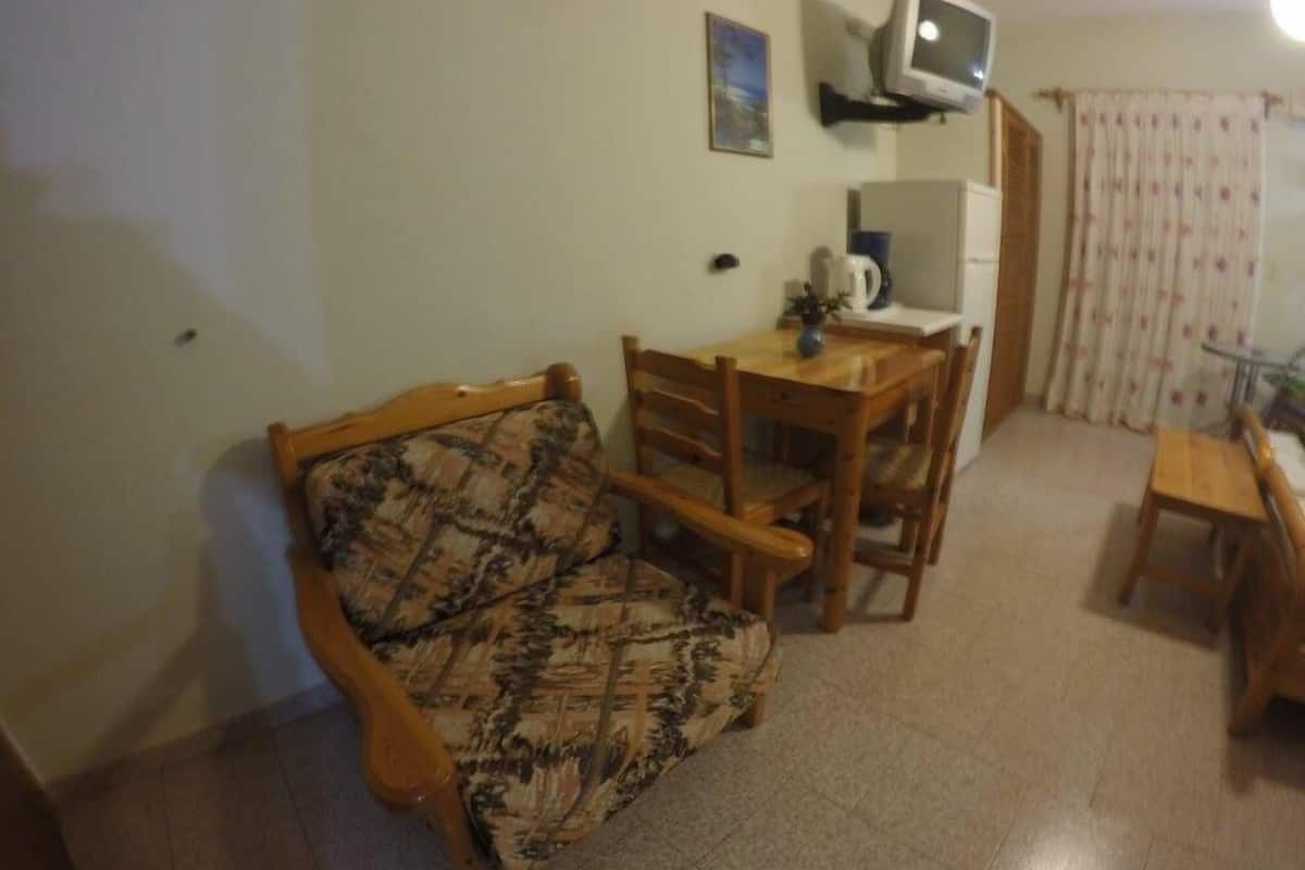 A small, cozy living room with a sofa, a wooden dining table, and a television mounted on the wall.