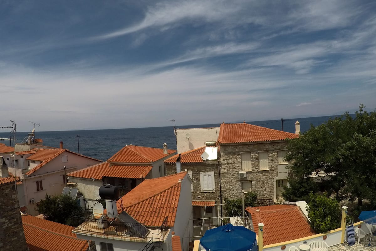 A coastal residential area with terracotta-tiled roofs, stone buildings, and a view of the sea.