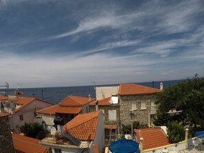 A coastal residential area with terracotta-tiled roofs, stone buildings, and a view of the sea.