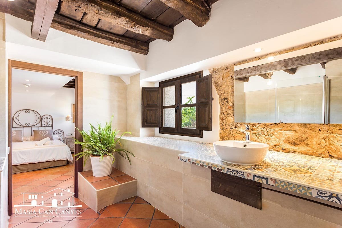 A bathroom with a stone wall, a large sink, and a window with wooden shutters.