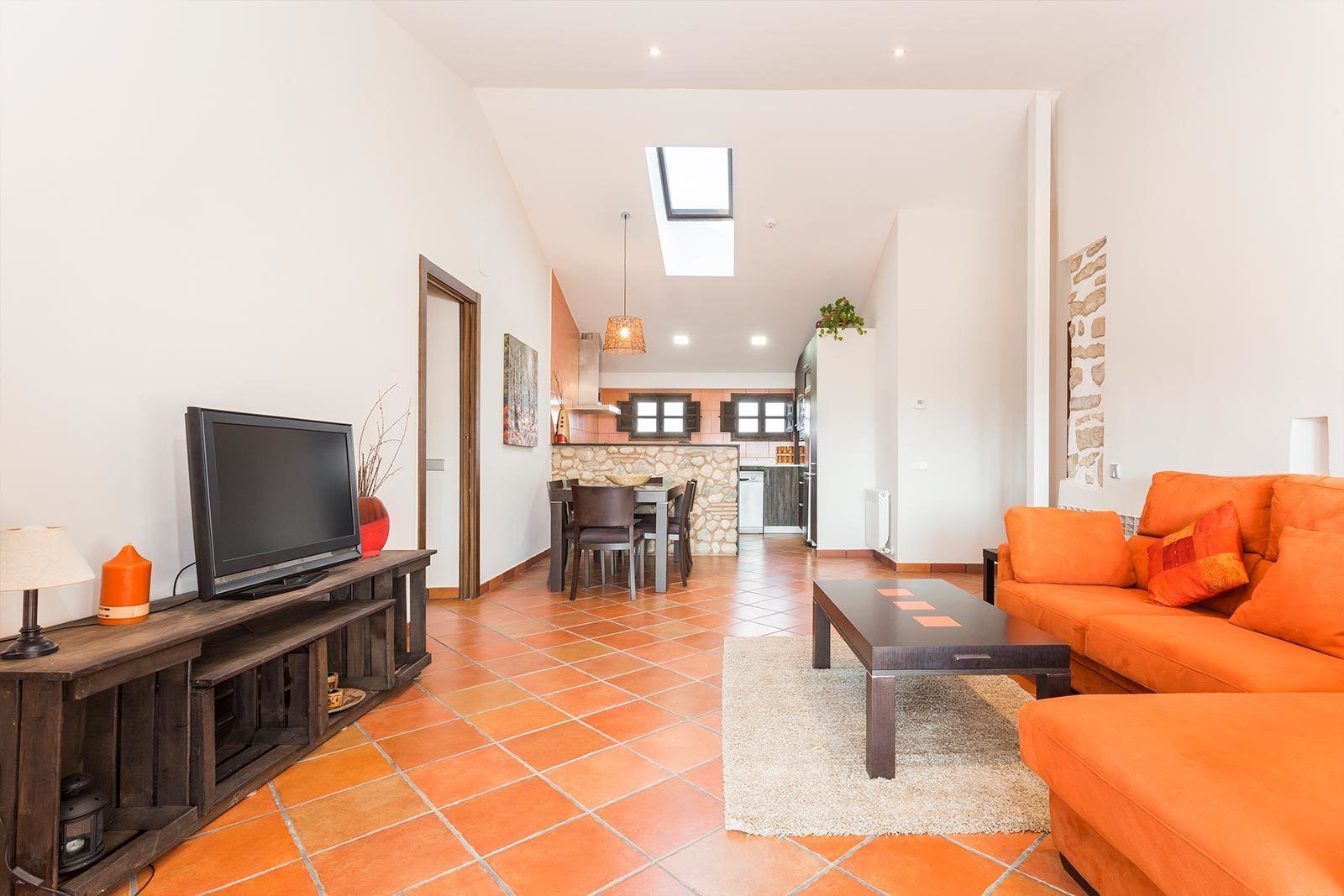 A modern living room with a TV, orange sofa, and a dining area with chairs and a table.
