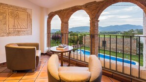 A balcony with a view of a swimming pool and mountains, furnished with two chairs and a small table. - Masia Can Canyes & Spa (Sant Llorenc d'Hortons)