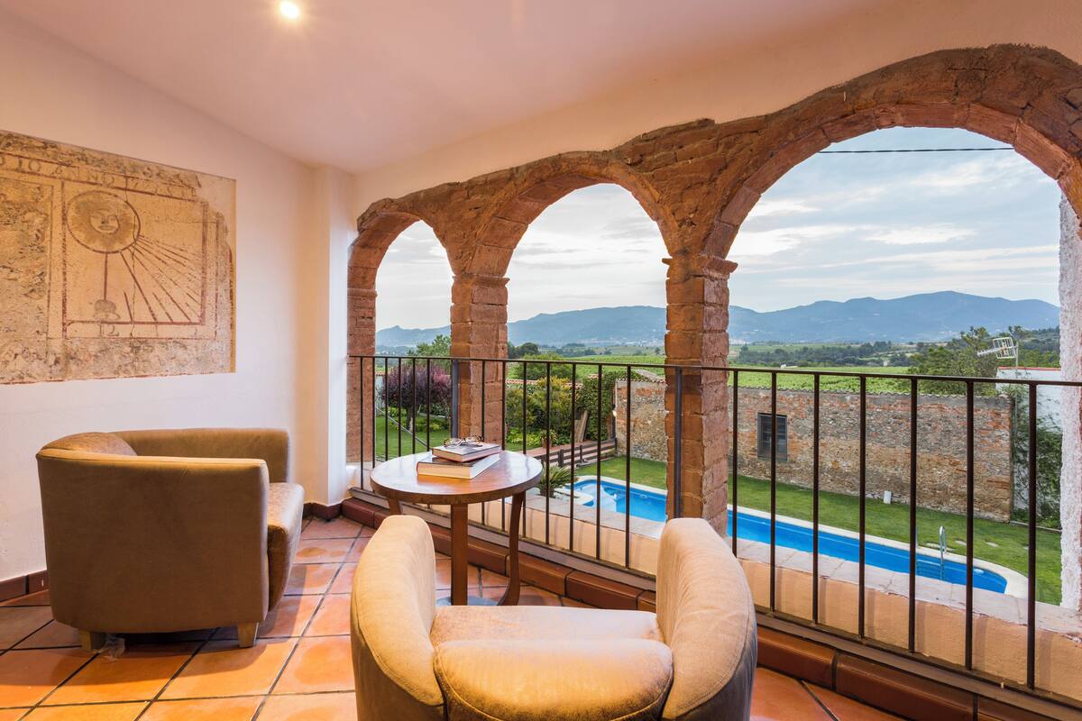 A balcony with a view of a swimming pool and mountains, furnished with two chairs and a small table.