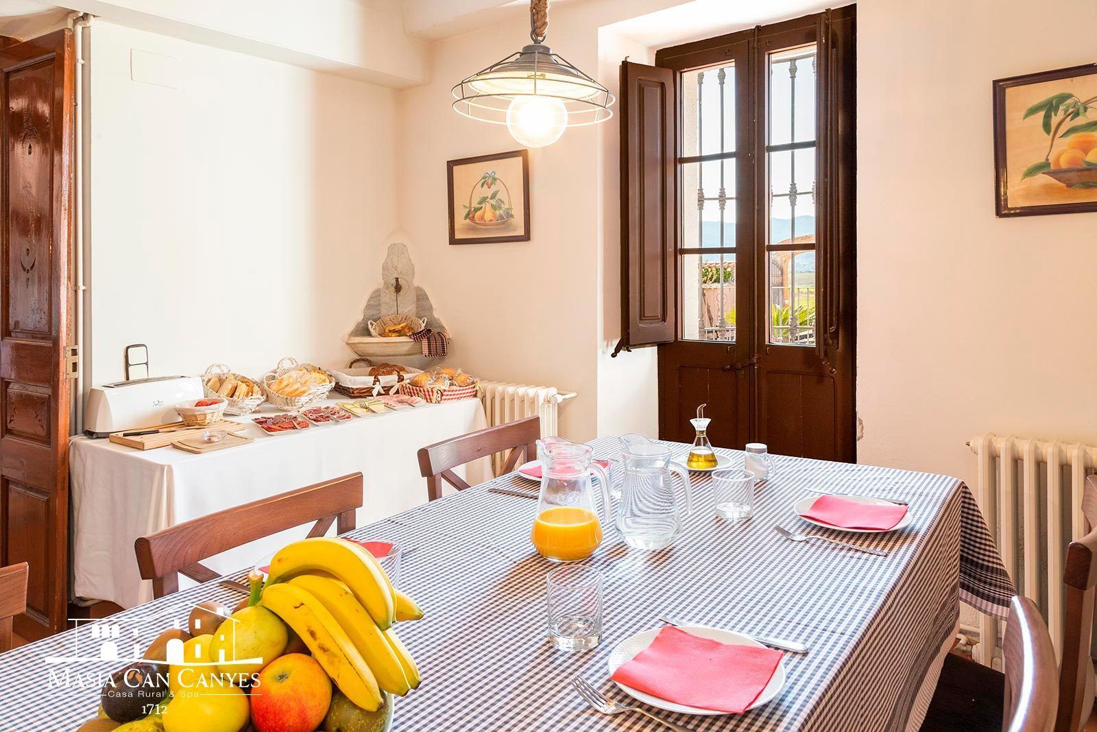 A dining area with a table set for breakfast, including fruits, bread, and a toaster.