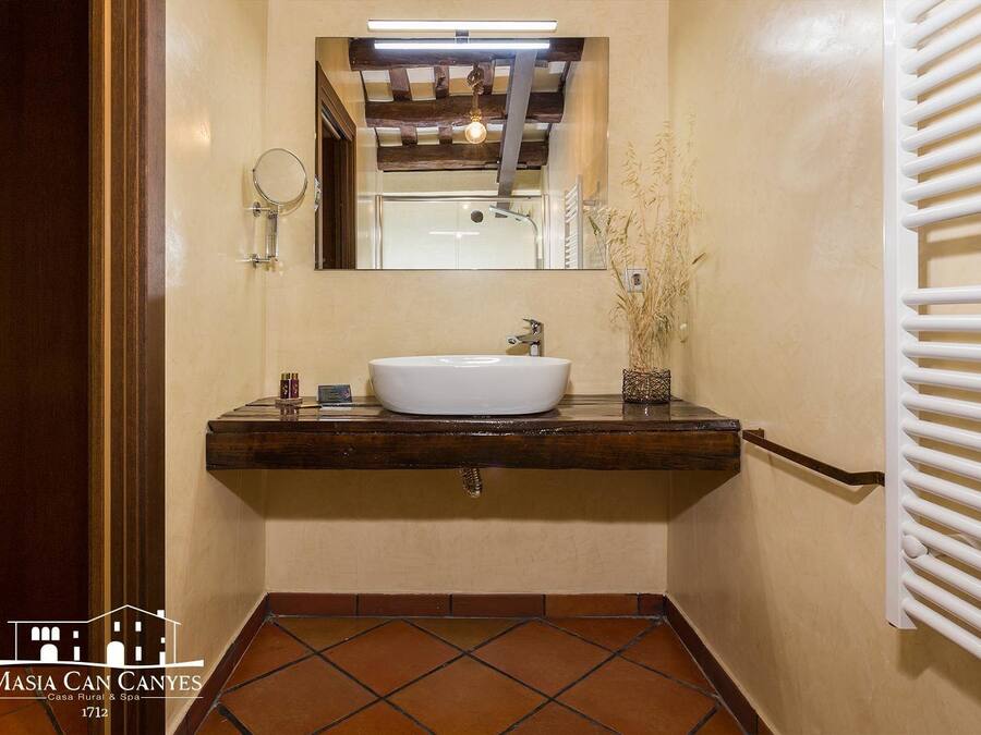 A bathroom with a white sink, wooden countertop, and a mirror above it. There is a towel rack on the wall and a small plant on the countertop.