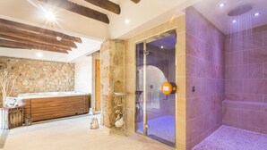 A bathroom with a stone wall, a wooden vanity, and a glass shower enclosure. - Masia Can Canyes & Spa (Sant Llorenc d'Hortons)