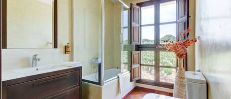 A bathroom with a large mirror, a bathtub, a toilet, and a window with a view of trees.