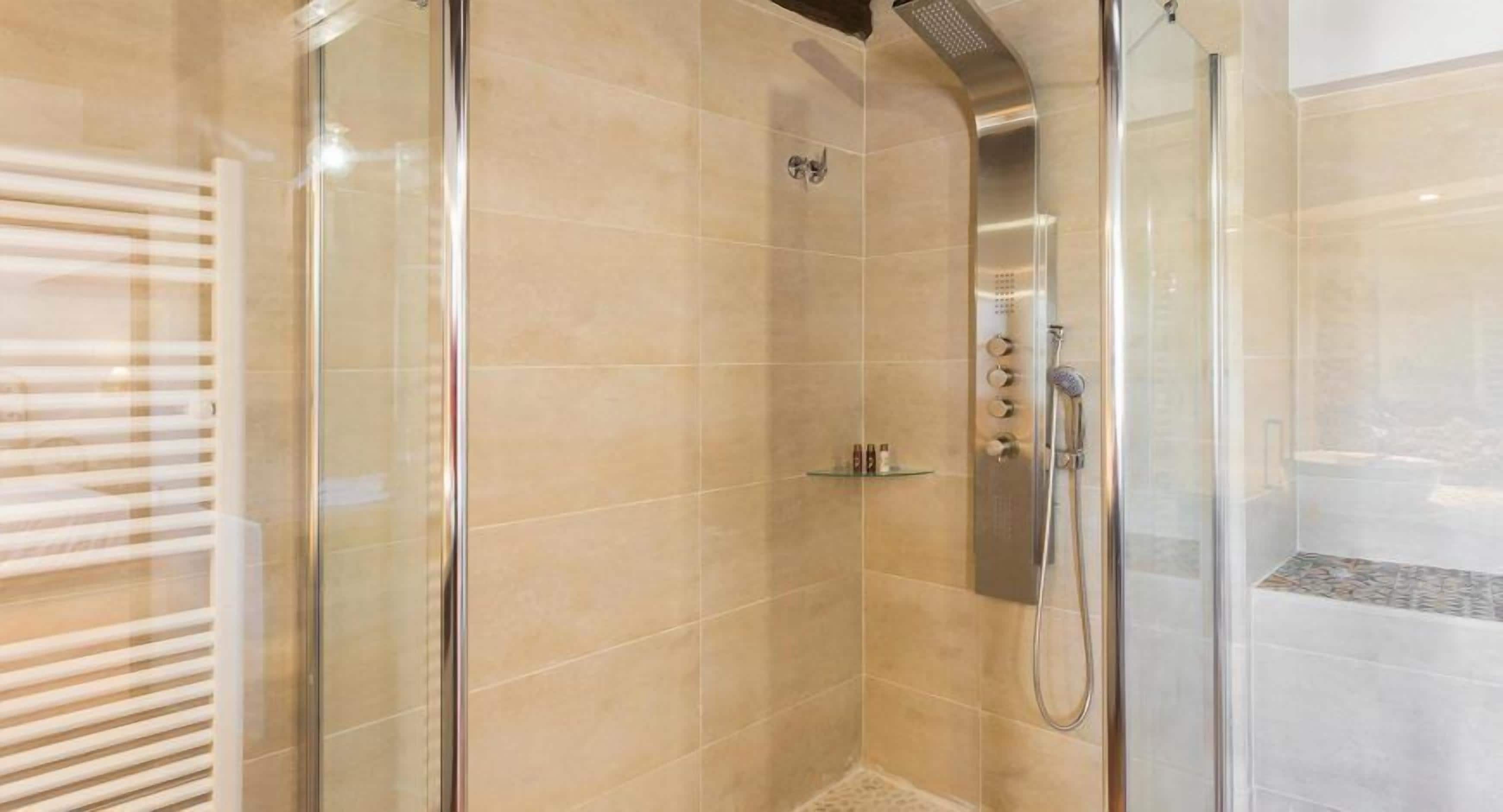 Une douche fermée par des parois en verre, dotée d’un pommeau de douche à main et d’un panneau de commande fixé au mur.