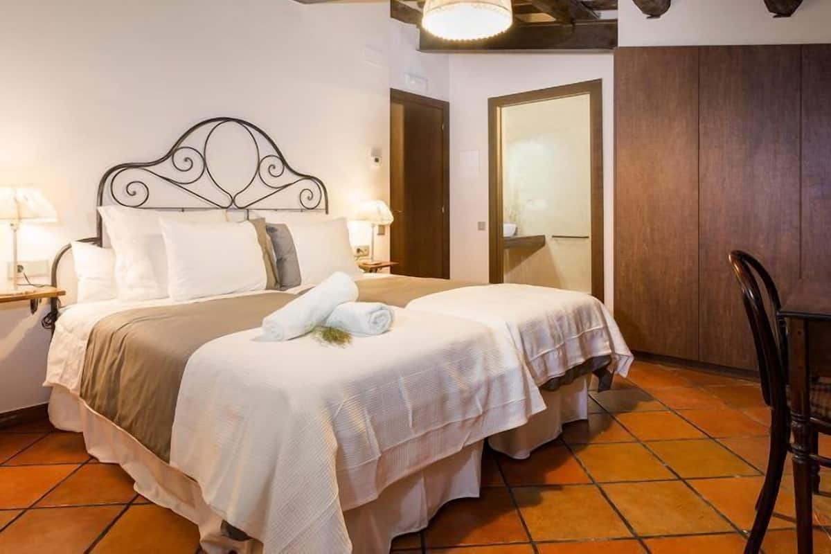 A double bed with a headboard, two bedside tables with lamps, a chair, and a wooden wardrobe.