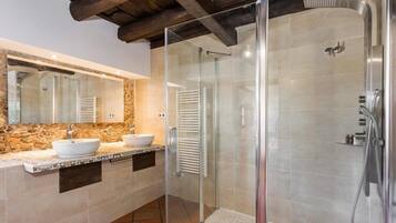 A modern bathroom with a stone backsplash, a large mirror, two sinks, and a glass-enclosed shower area.