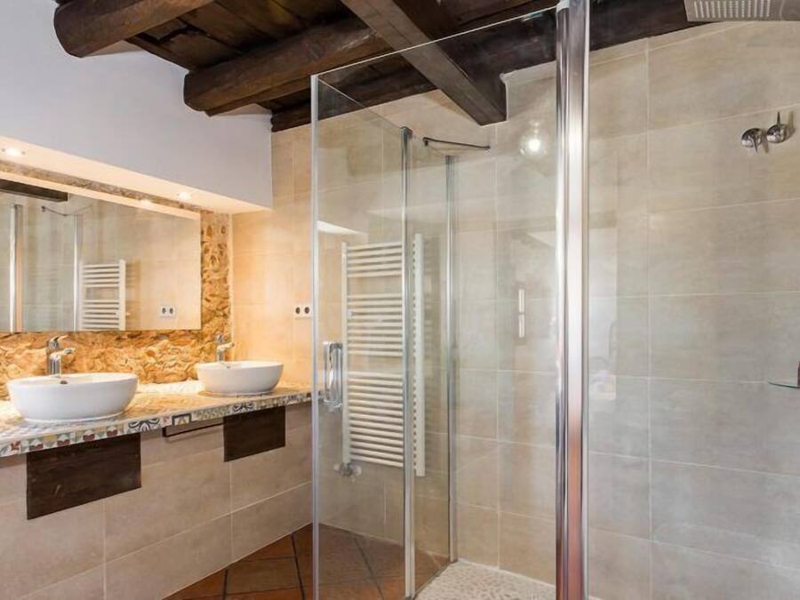 A modern bathroom with a stone backsplash, a large mirror, two sinks, and a glass-enclosed shower area.