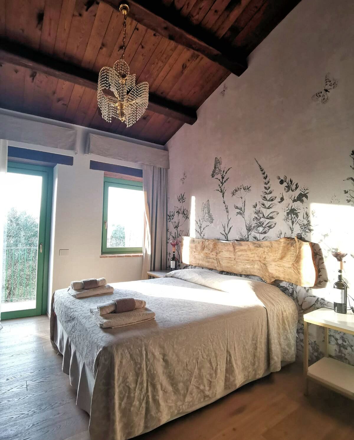 A bedroom with a large bed, wooden ceiling, and a floral wall mural.
