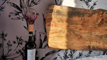 Une tête de lit en bois se détache sur un fond de papier peint à motifs floraux, et une bouteille de vin est posée sur une table de chevet.