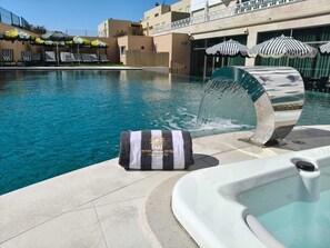 A swimming pool with lounge chairs and umbrellas, a hot tub, and a towel with a logo. - Aurea Fátima Hotel Congress & Spa (Ourem)
