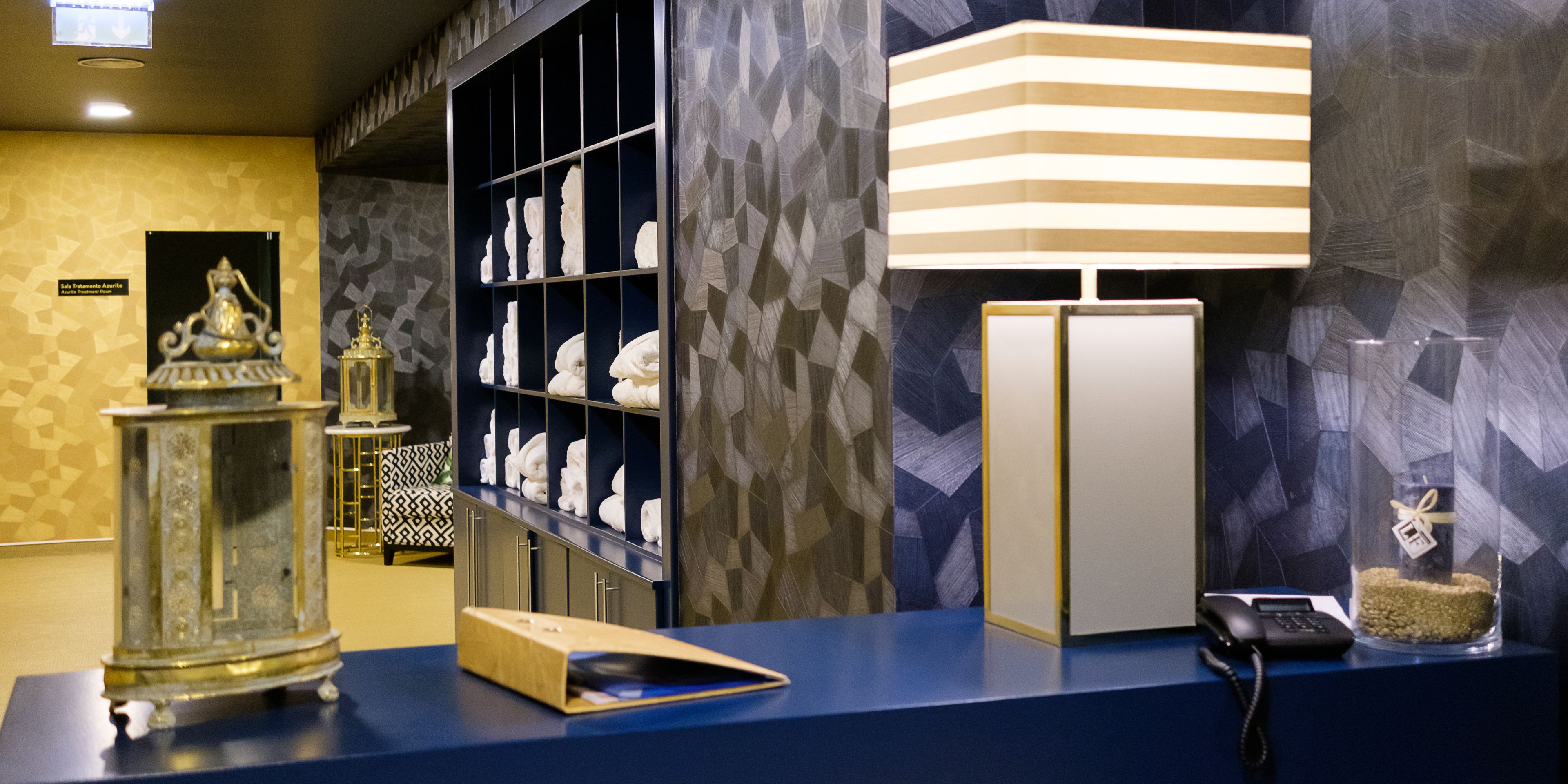 A reception desk with a telephone, a glass display case with a decorative item, and a wall with geometric patterns.