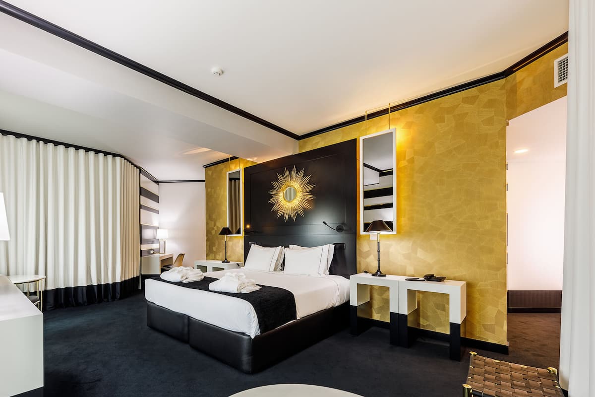 A modern hotel room with a large bed, bedside tables, a desk, and a mirror.