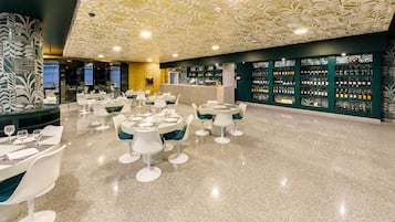A modern restaurant with round tables and white chairs, a polished floor, and a wall of wine bottles.