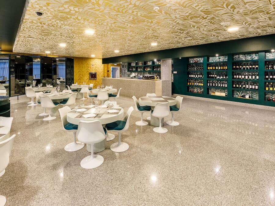 A modern restaurant with round tables and white chairs, a polished floor, and a wall of wine bottles.