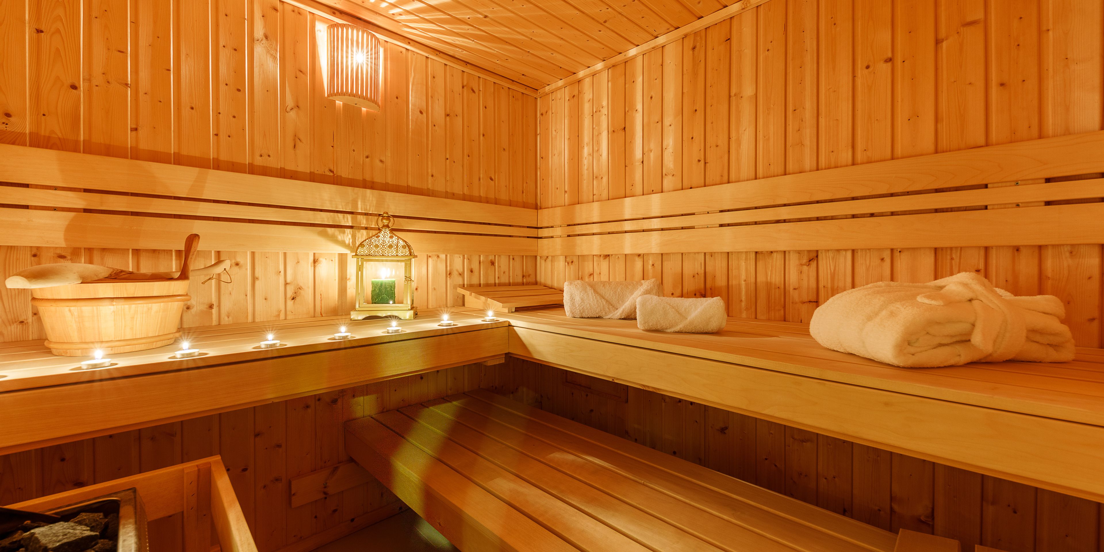 A wooden sauna with benches, a bucket, and a lantern.