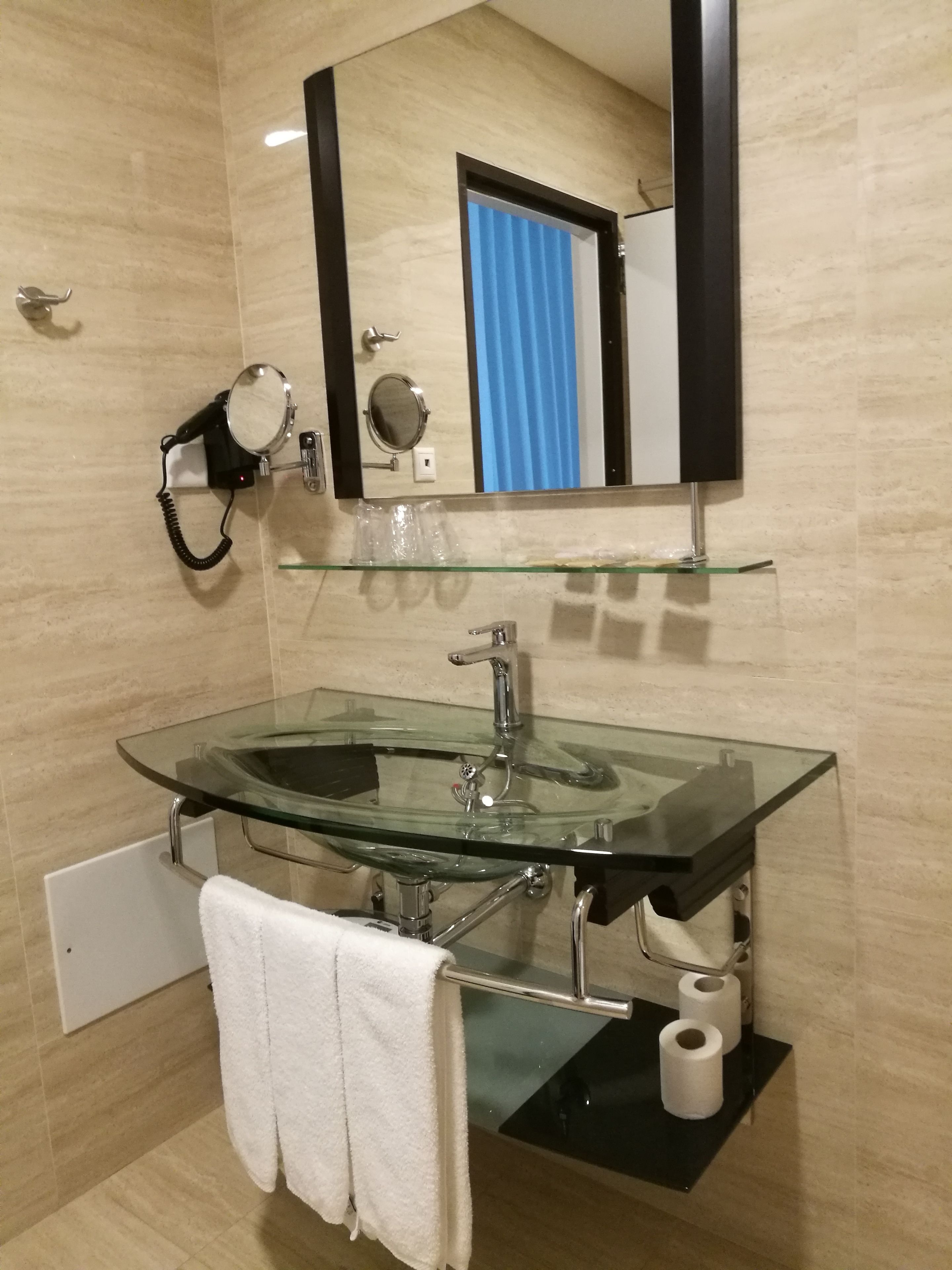 A modern bathroom with a glass sink, a towel rack, a mirror, and a toilet paper holder.
