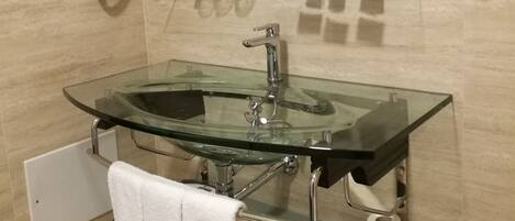 A modern bathroom with a glass sink, a towel rack, a mirror, and a toilet paper holder.