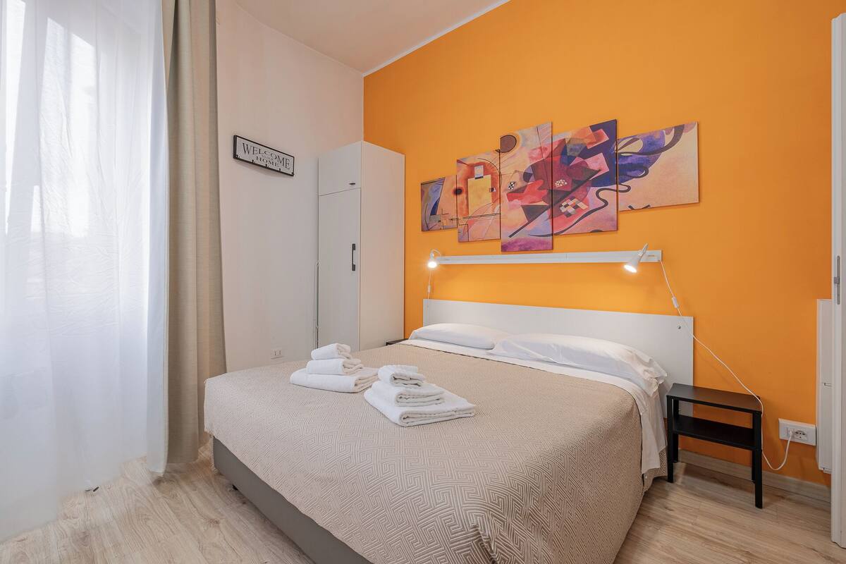 Ein Schlafzimmer mit einem Bett, einem Nachttisch, einer Wandlampe und einem Gemälde.