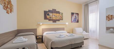 A hotel room with two beds, a bedside table, a chair, and artwork on the walls.