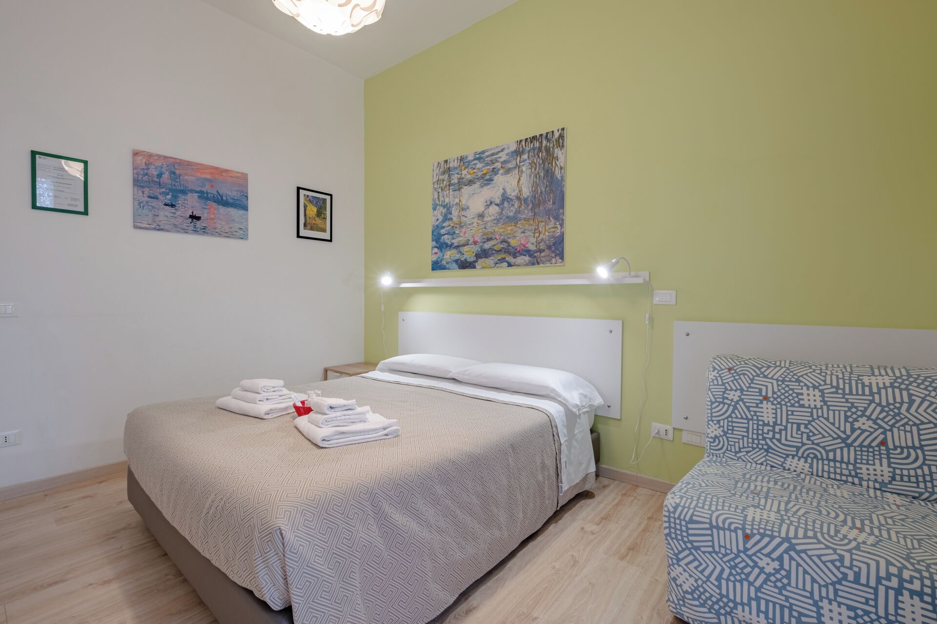 Une chambre d’hôtel avec un lit, une chaise et trois tableaux accrochés au mur.