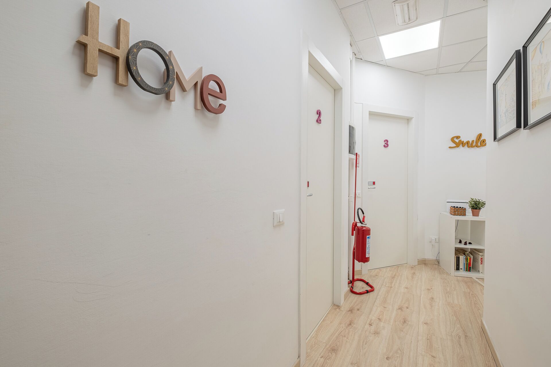 A hallway with a 'Home' sign, a fire extinguisher, and a 'Smile' sign on the wall.