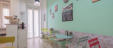 A cozy kitchen with a dining area, featuring a green wall, wooden flooring, and a variety of kitchen utensils and decorations.