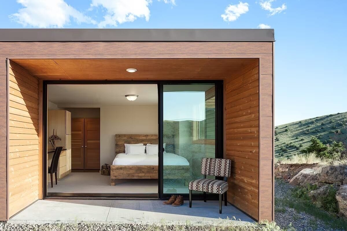 A modern bedroom with a large bed, a chair, and a sliding glass door leading to a balcony.