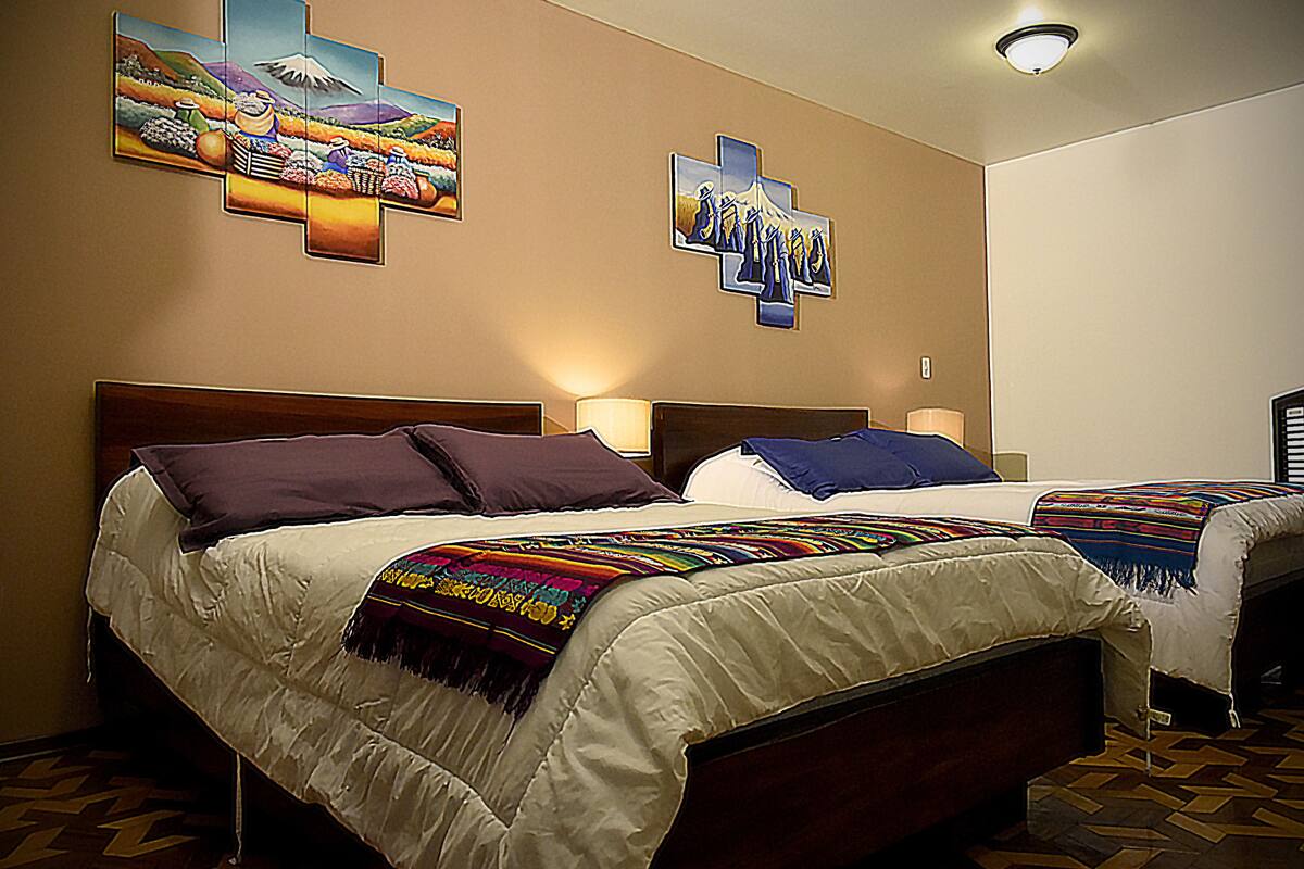 A hotel room with two beds, a large cross artwork on the wall, and a patterned floor.