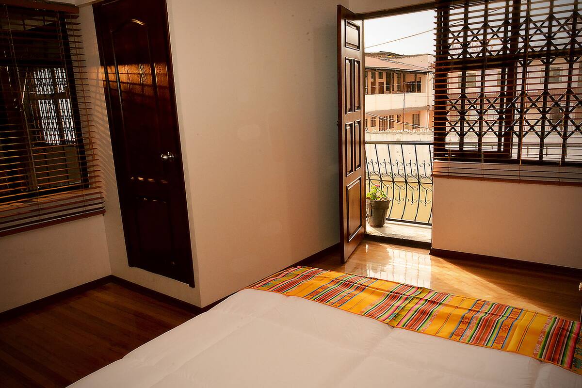 A hotel room with a bed, a window with metal bars, and a view of buildings outside.