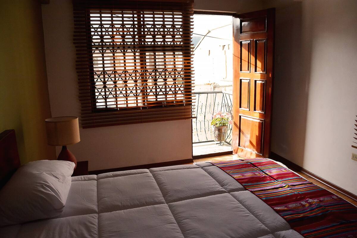 A bedroom with a bed, a window with blinds, and a door leading to a balcony.