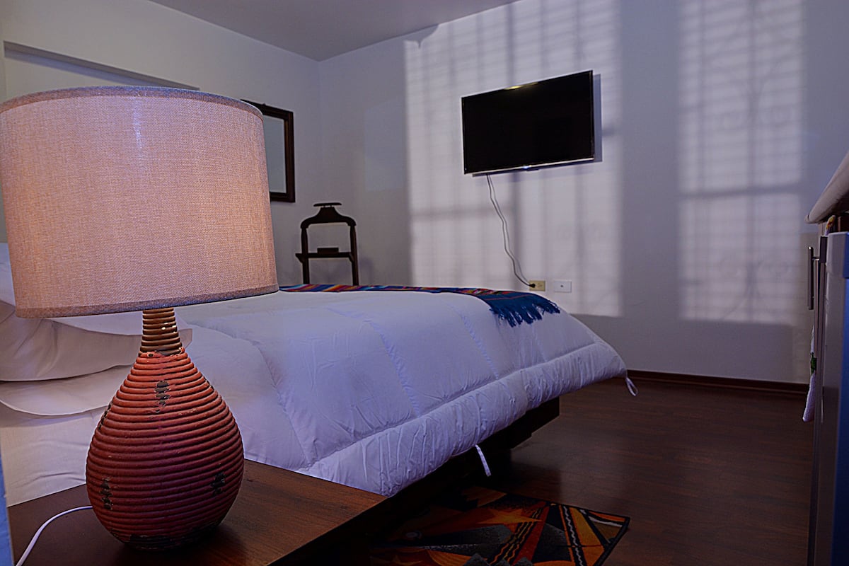 A bedroom with a bed, a lamp, a TV, and a window.