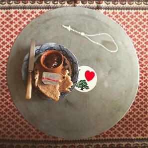Uma mesa redonda com um prato de pão e uma pequena tigela de geleia, uma faca e um objeto decorativo com um coração e uma árvore.