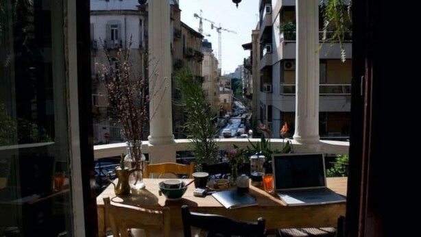 En balkon med et bord, stole, en bærbar computer og en hængende lygte.