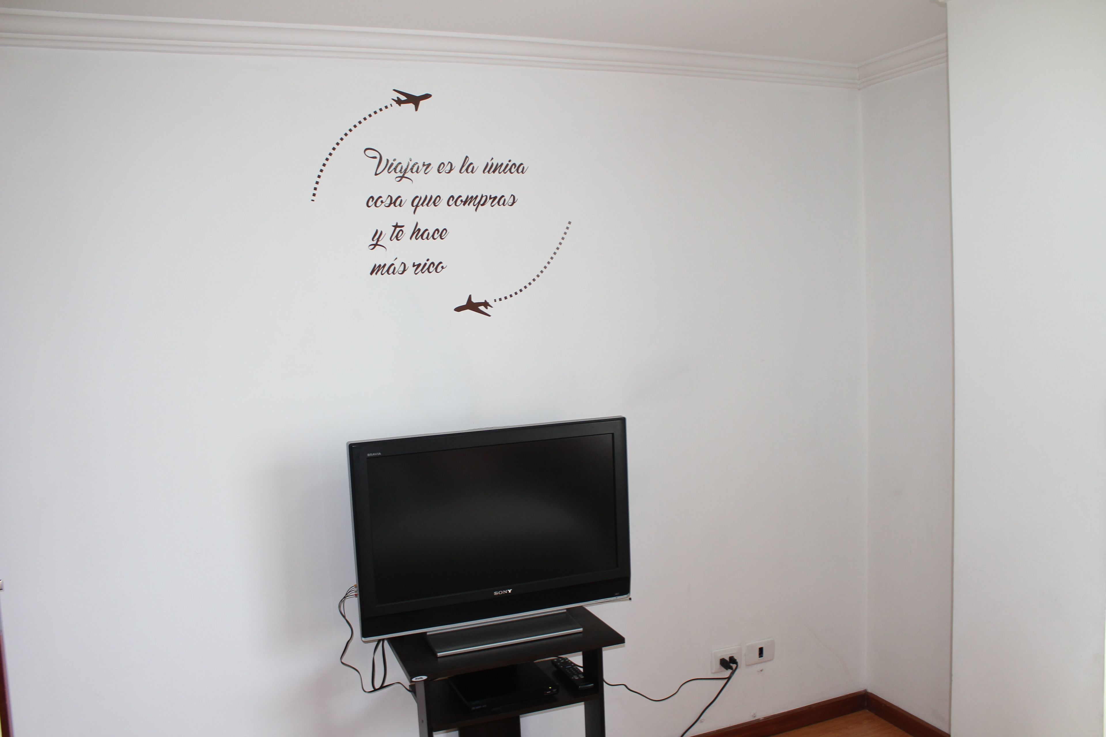 A room with a flat-screen TV on a stand, a wall with a decorative sticker, and a power outlet.