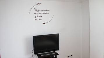 A room with a flat-screen TV on a stand, a wall with a decorative sticker, and a power outlet.