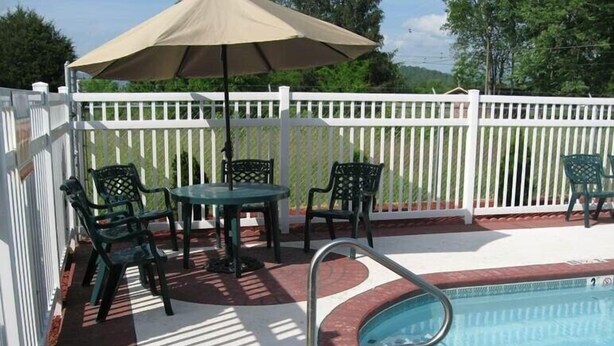 A pool area with a white fence, a table with chairs, and a pool with a ladder. - Mountain Inn & Suites Dunlap (Dunlap)