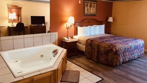 A hotel room with a large bed, a separate bathroom with a bathtub, a desk with a chair, a television, and a framed picture on the wall. - Mountain Inn & Suites Dunlap (Dunlap)