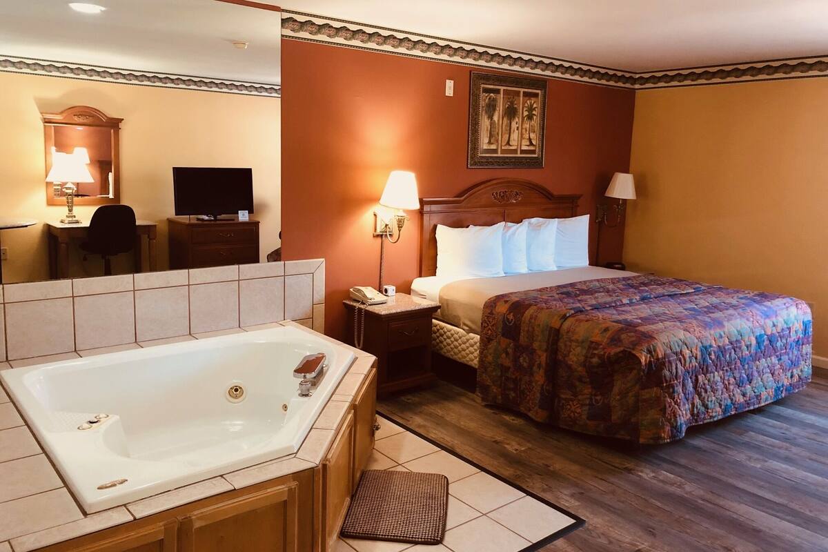 Habitación de hotel con una cama grande, baño independiente con bañera, escritorio con silla, televisión y un cuadro enmarcado en la pared.