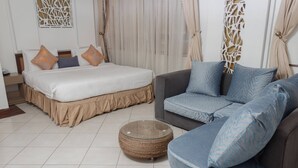 Una habitación de hotel con cama, sofá y un otoman redonda.