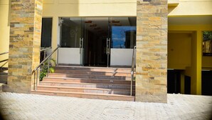 Entrada de hotel con pilares de piedra, puertas de cristal y una escalera que conduce al interior.