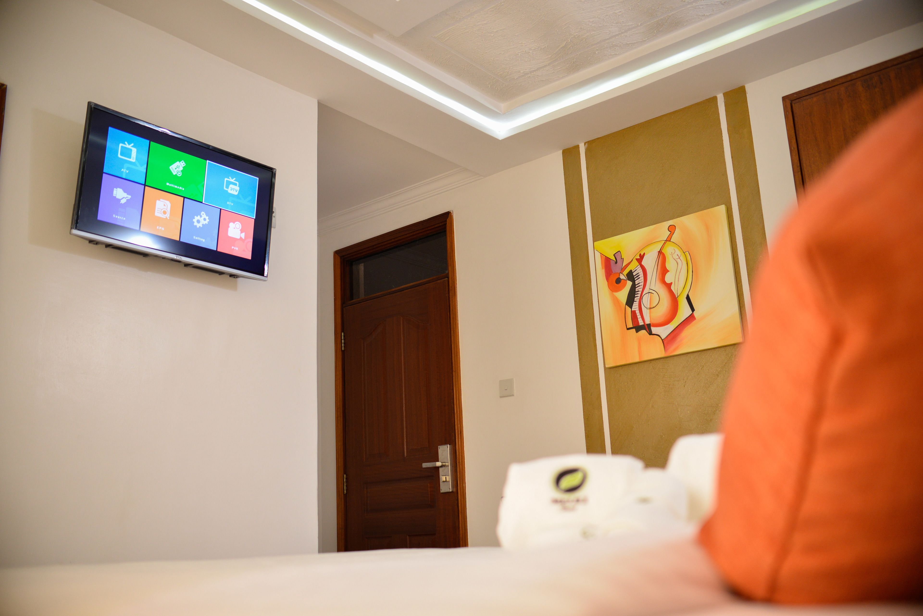 Habitación de hotel con televisor de pantalla plana mostrando una interfaz de colores, una puerta de madera y un cuadro en la pared.