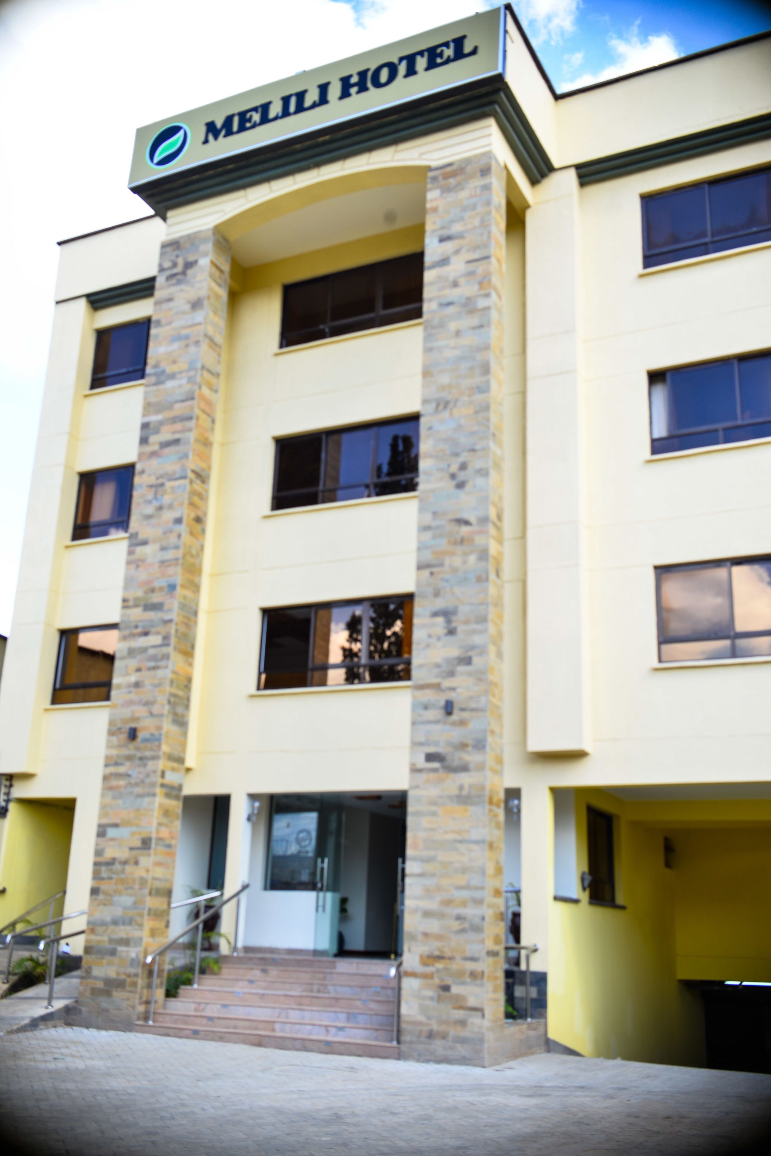 A hotel with a sign reading "MELILI HOTEL". It has multiple floors with windows and a central entrance with steps.