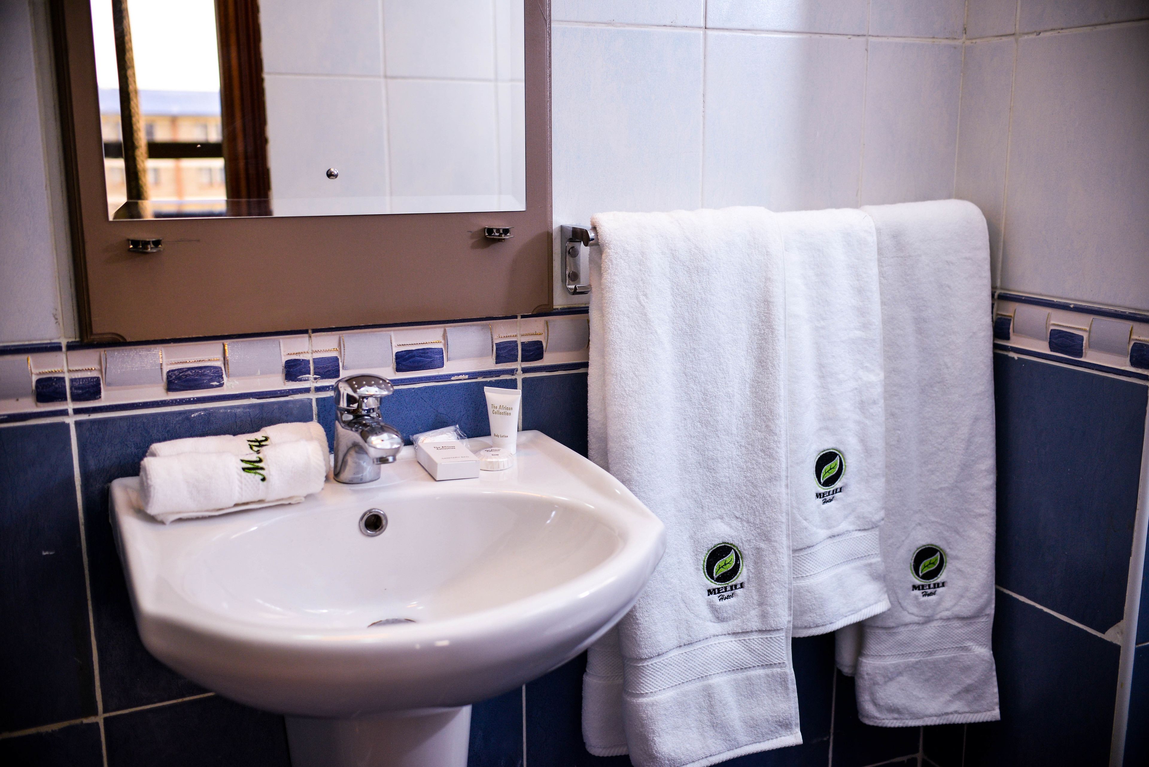 Une salle de bain avec un lavabo blanc, un miroir et deux serviettes suspendues à un porte-serviettes.