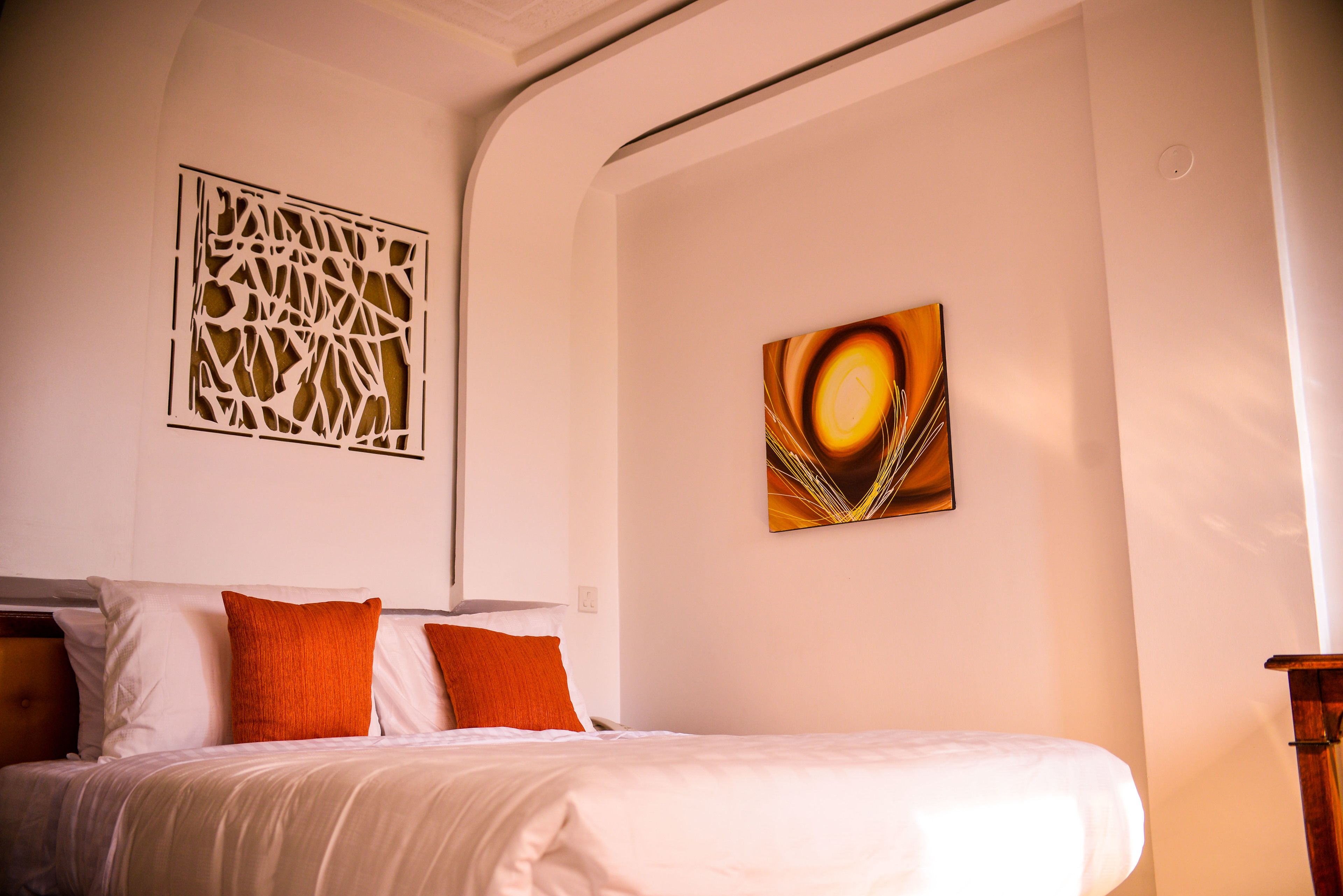 A hotel room with a neatly made bed, a decorative wall panel, and a framed artwork.