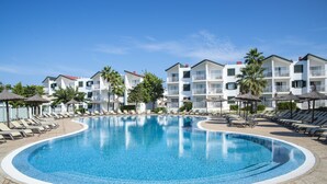 A swimming pool surrounded by lounge chairs and umbrellas, with multi-story buildings in the background. - Pierre & Vacances Menorca Cala Blanes (Ciutadella de Menorca)
